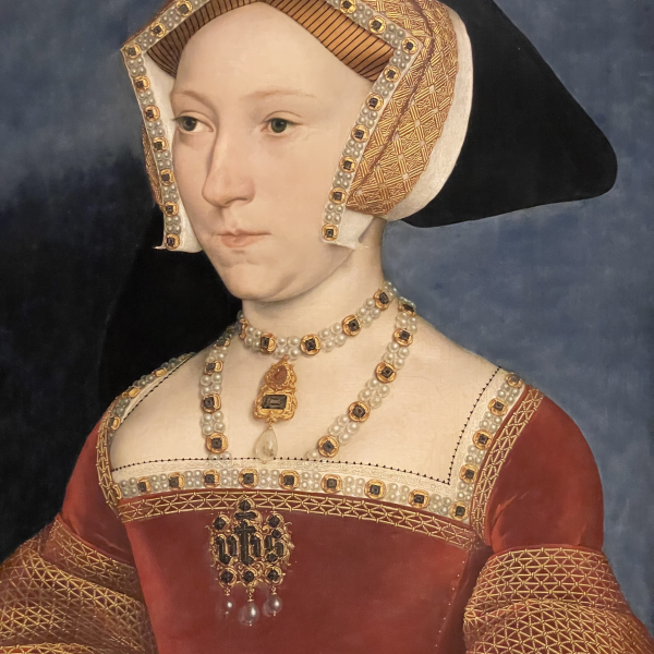 A picture of Hans Holbein's portrait of Jane Seymour. The photograph is of the top half of the portrait. Jane Seymour is depicted wearing a red and gold dress, a gold and black headpiece, and ornate jewelry.