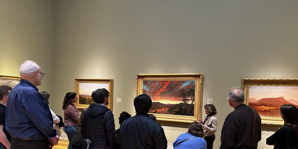 An image showing a group of students and faculty looking at Dr. Angela Miller, who is standing in front of Frederic Edwin Church's painting Twilight in the Wilderness